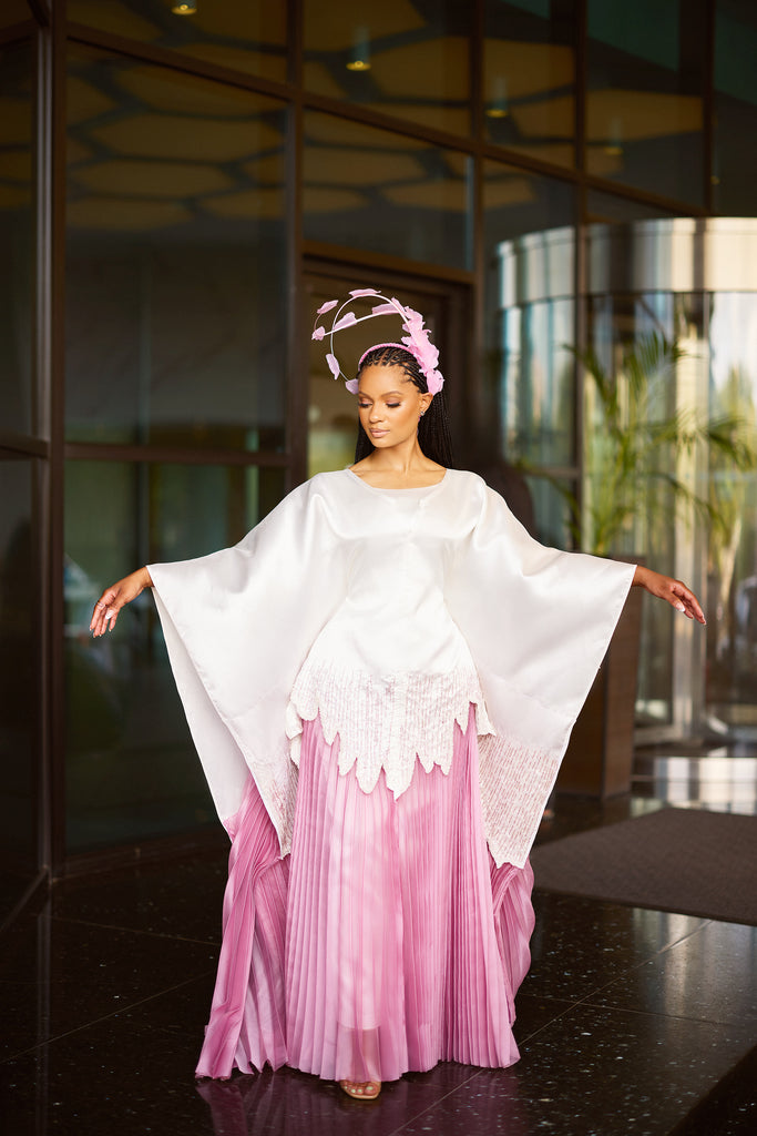 Andrea Crayton wearing satin agbada with hand-beaded scalloped edge layered over pleated white skirt, walking with grace and confidence.