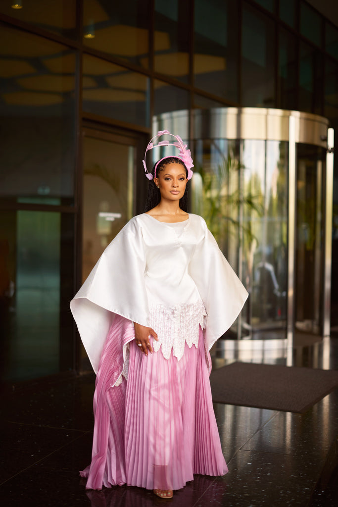 Andrea Crayton wearing satin agbada with hand-beaded scalloped edge layered over pleated white skirt, walking with grace and confidence.