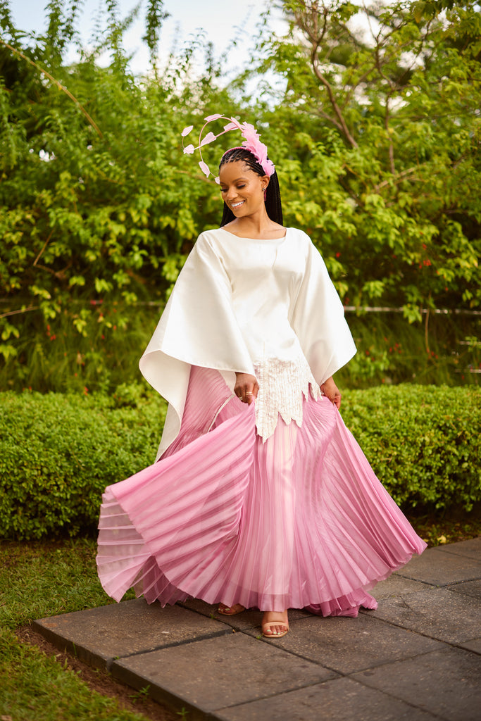 Andrea Crayton wearing satin agbada with hand-beaded scalloped edge layered over pleated white skirt, walking with grace and confidence.